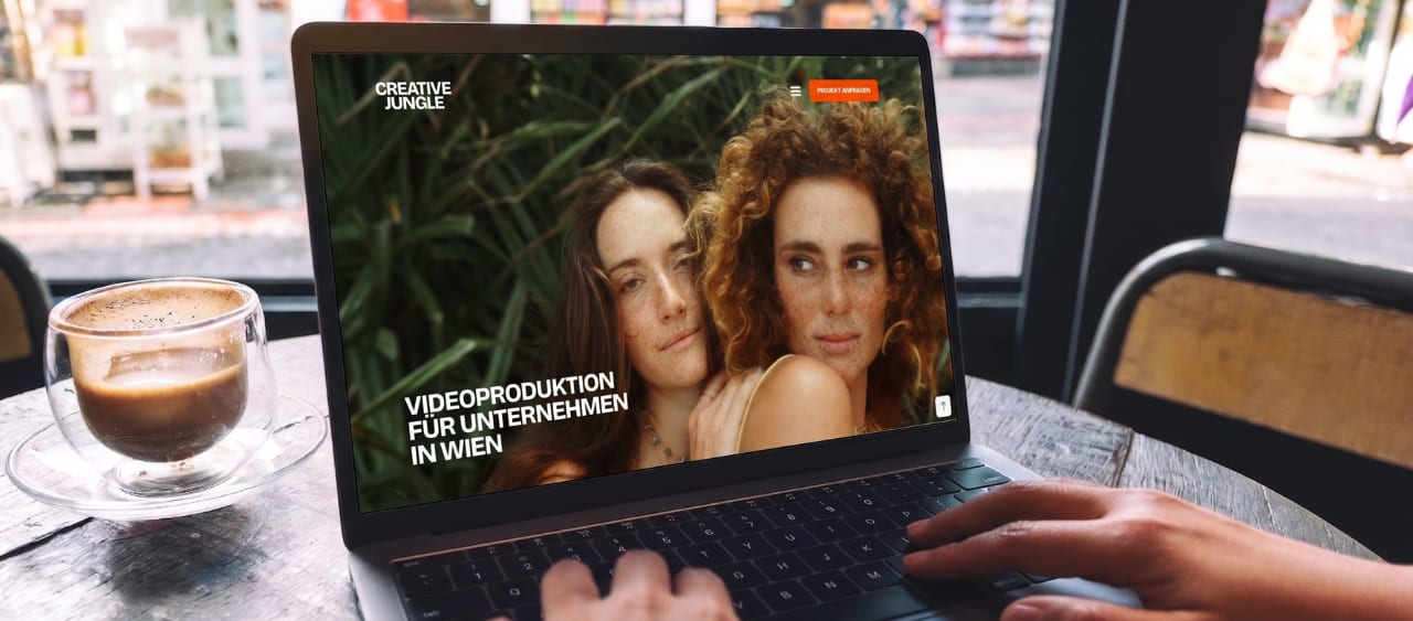 Ein Laptop auf einem Kaffeetisch zeigt die neu gestaltete, moderne Website von Creative Jungle mit einem hochauflösenden Video-Header zum Thema „Videoproduktion für Unternehmen in Wien“.